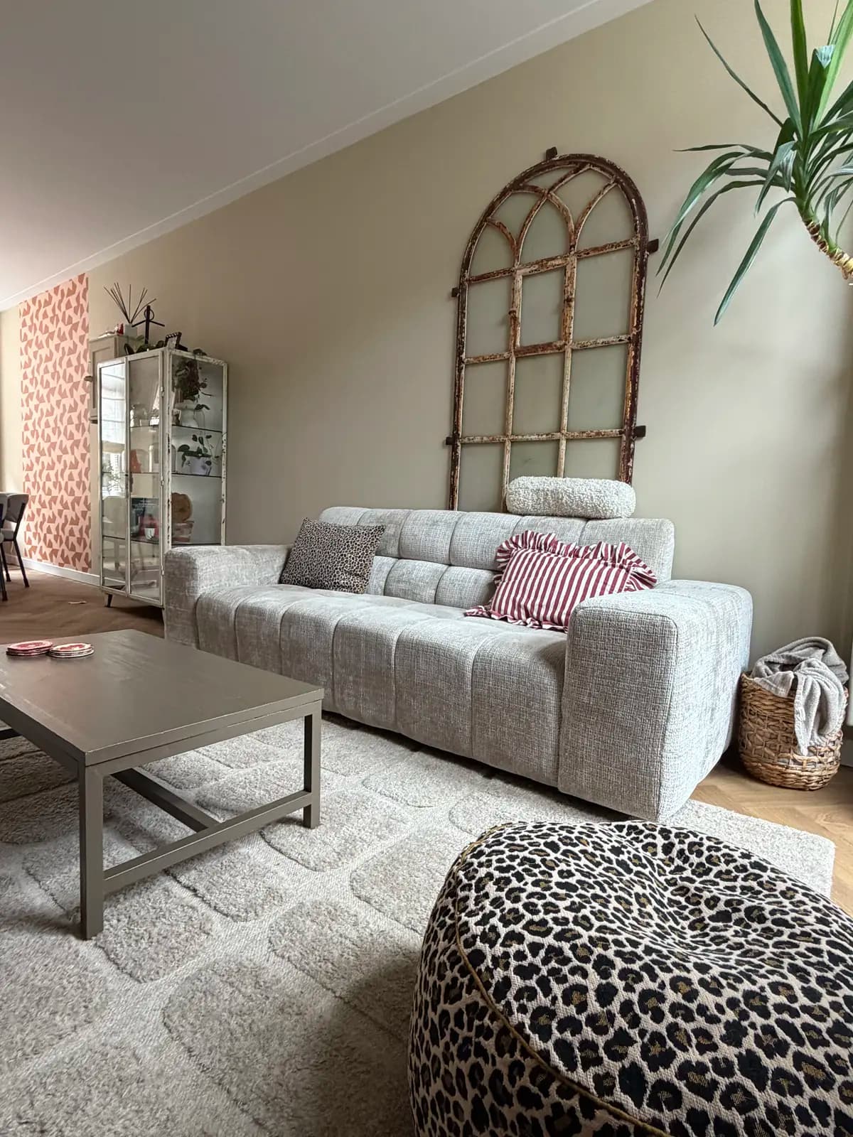 Woonkamer na de make-over, met een lichte bouclé bank, oud raamkozijn aan de wand en een luipaardpoef