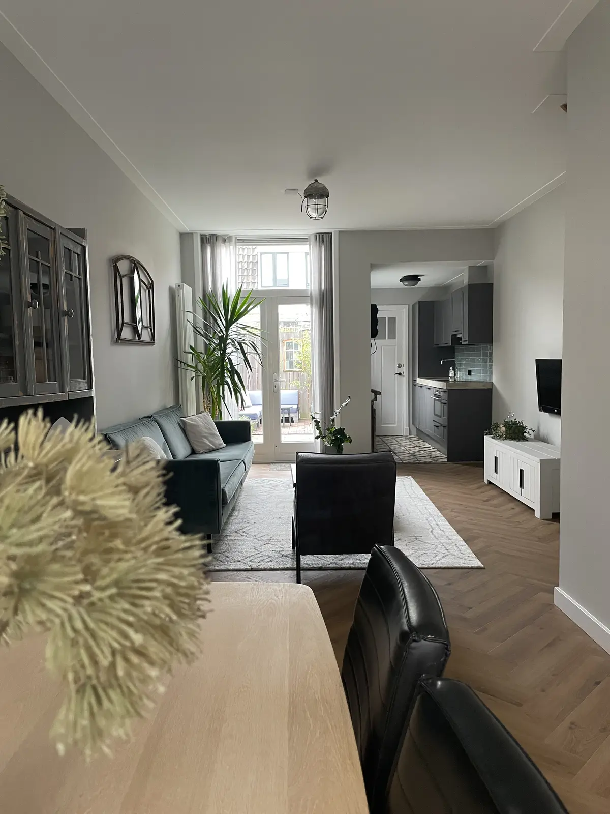 De woonkamer voor de make-over, met grijze wanden, een groene bank en zwarte stoelen