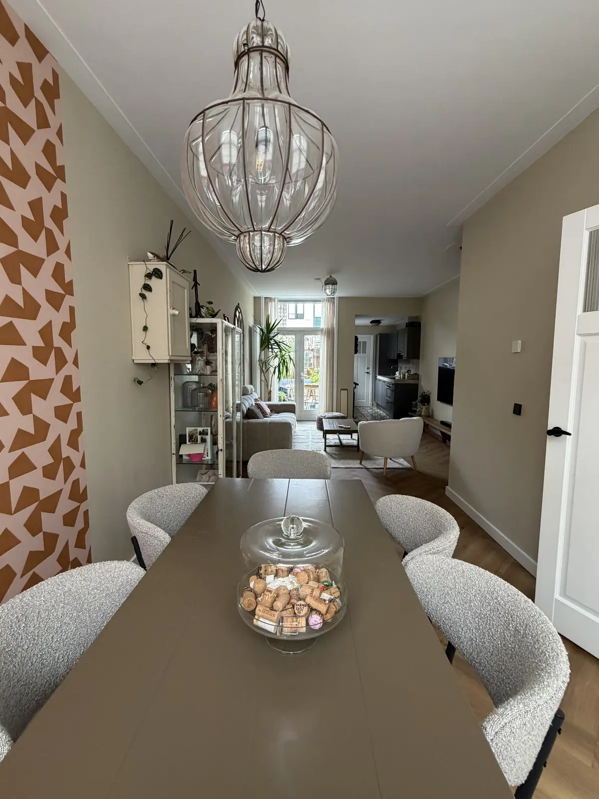 Dezelfde woonkamer na de make-over, met warme beige wanden, behang bij de eetkamer en bouclé stoelen