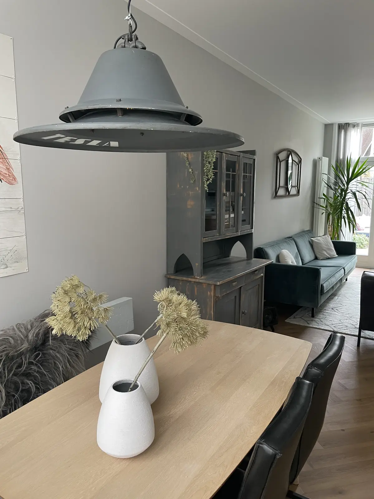 De eettafel voor de make-over: een lichte houten tafel met zwarte stoelen onder een grijze industriële lamp