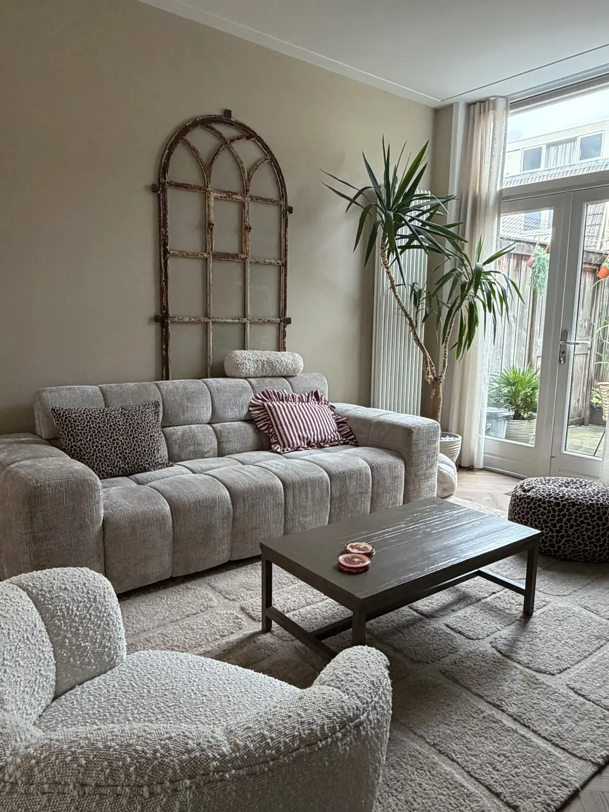 De zithoek na de make-over, met een lichte bouclé bank, fauteuil en het oude raamkozijn aan de wand