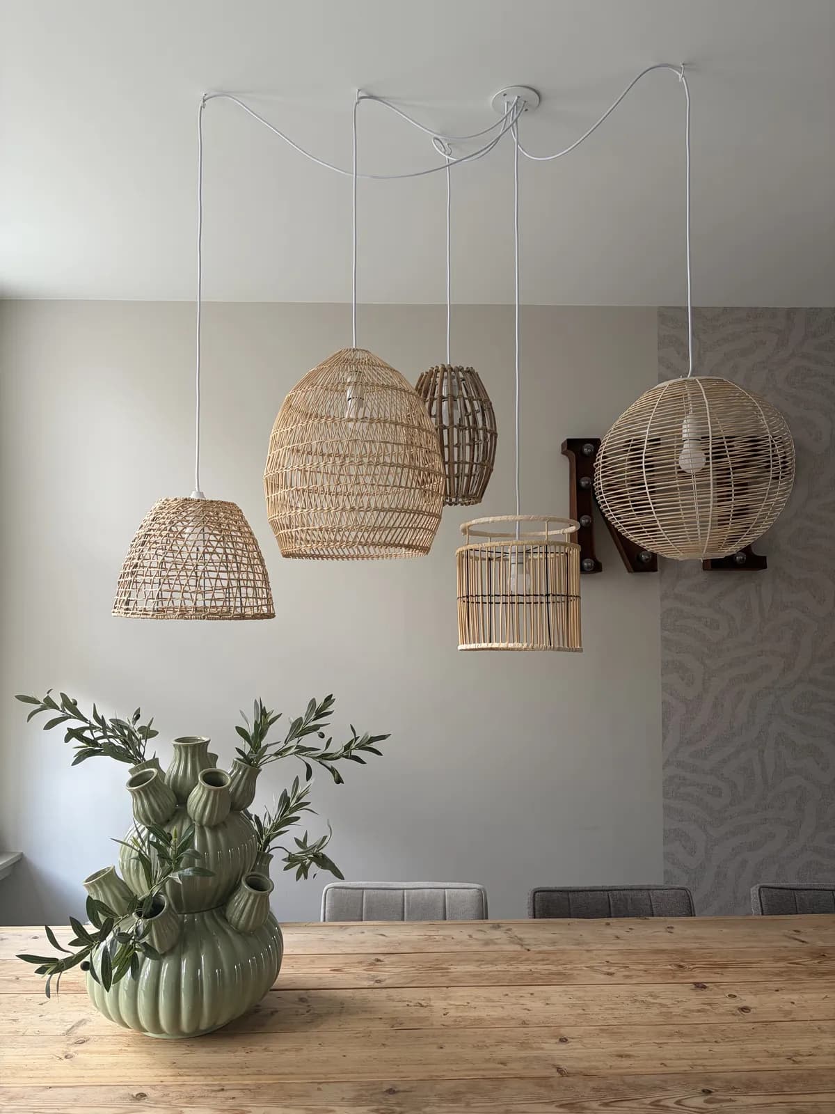 Zelfgemaakte hanglamp van vijf rieten en bamboe kappen aan witte snoeren boven de houten eettafel