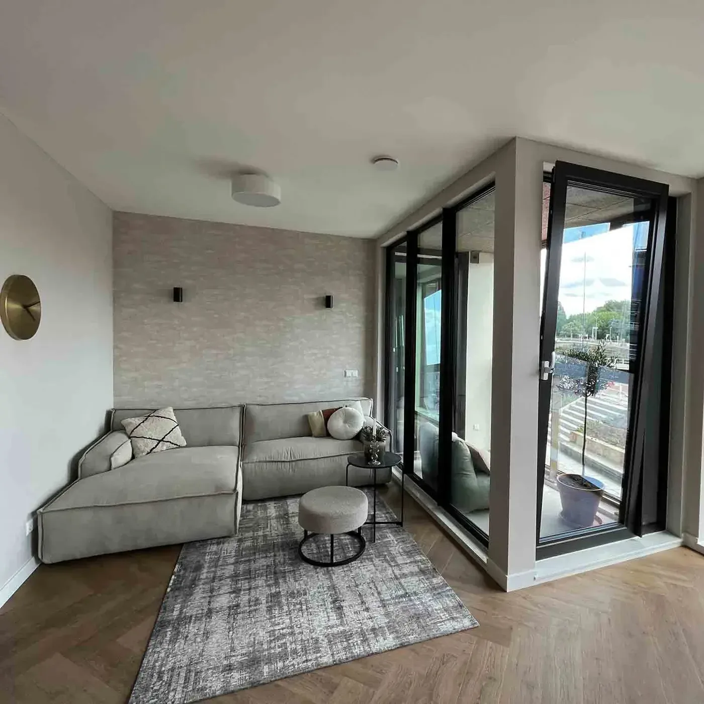 Woonkamer met lichte hoekbank en stalen puien naar het balkon