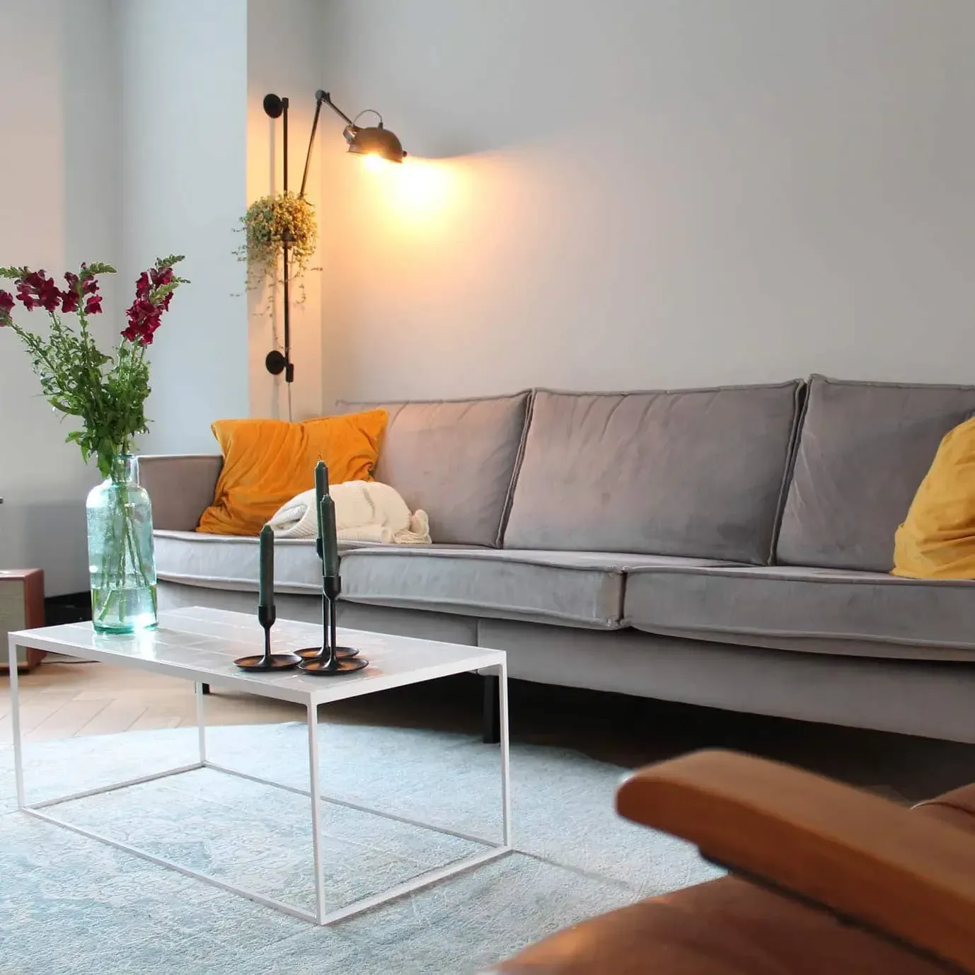 Lichte woonkamer met lange bank, okergele kussens en bloemen op tafel