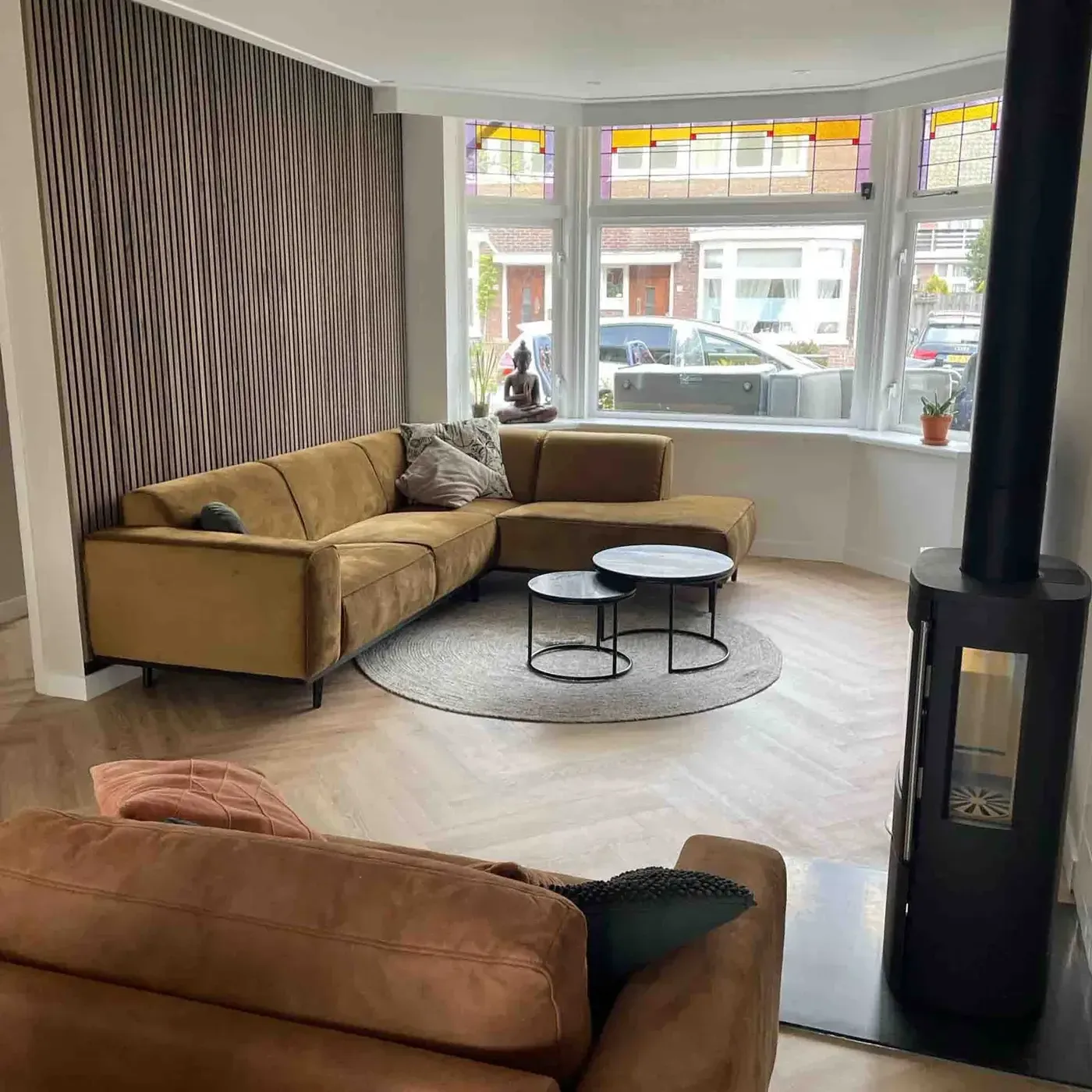 Woonkamer met okergele hoekbank, houten lattenwand en houtkachel