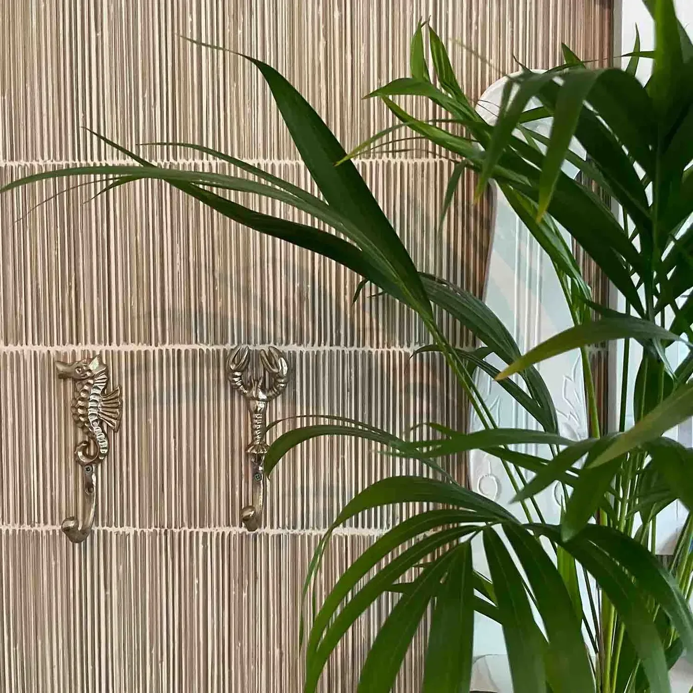 Detail van de lattenwand met messing haken en een palm ervoor