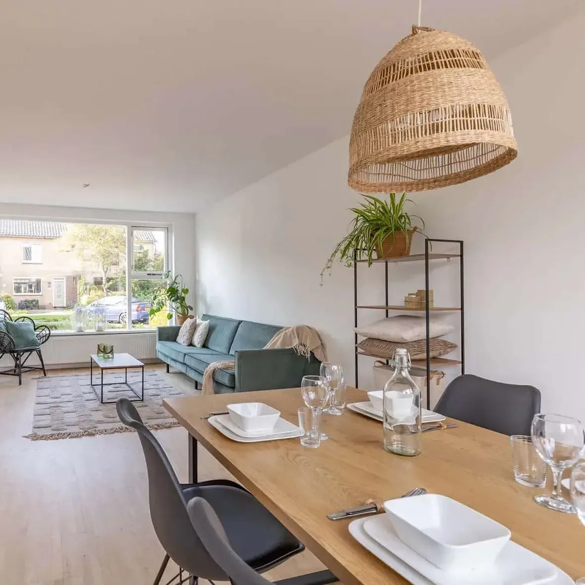 Gedekte eettafel onder een rieten hanglamp in een licht appartement