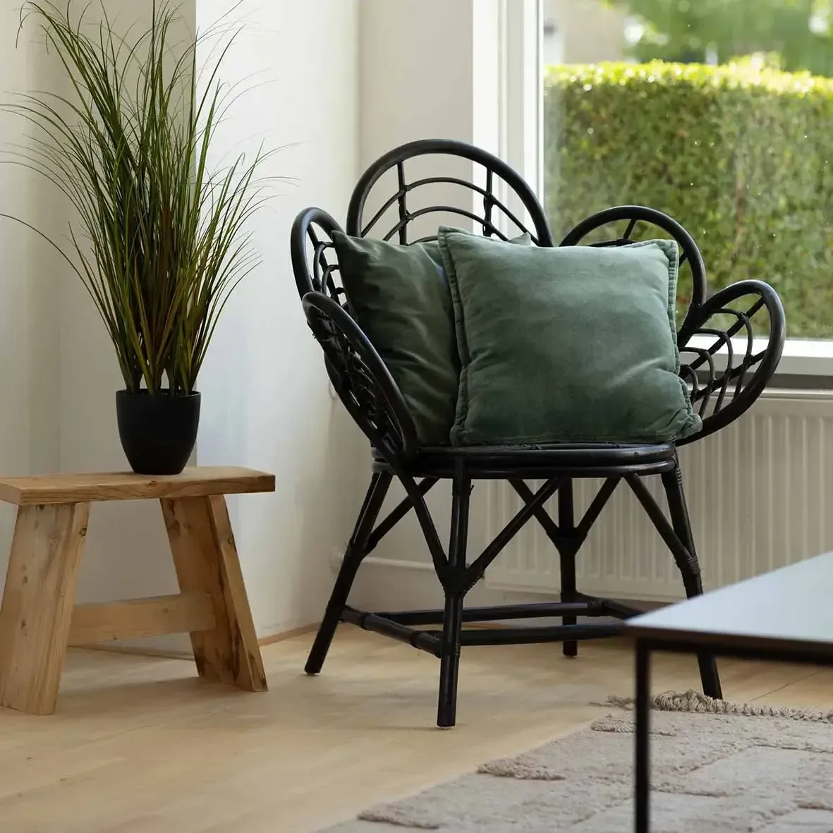 Zwarte rotanstoel met groen kussen naast een houten krukje