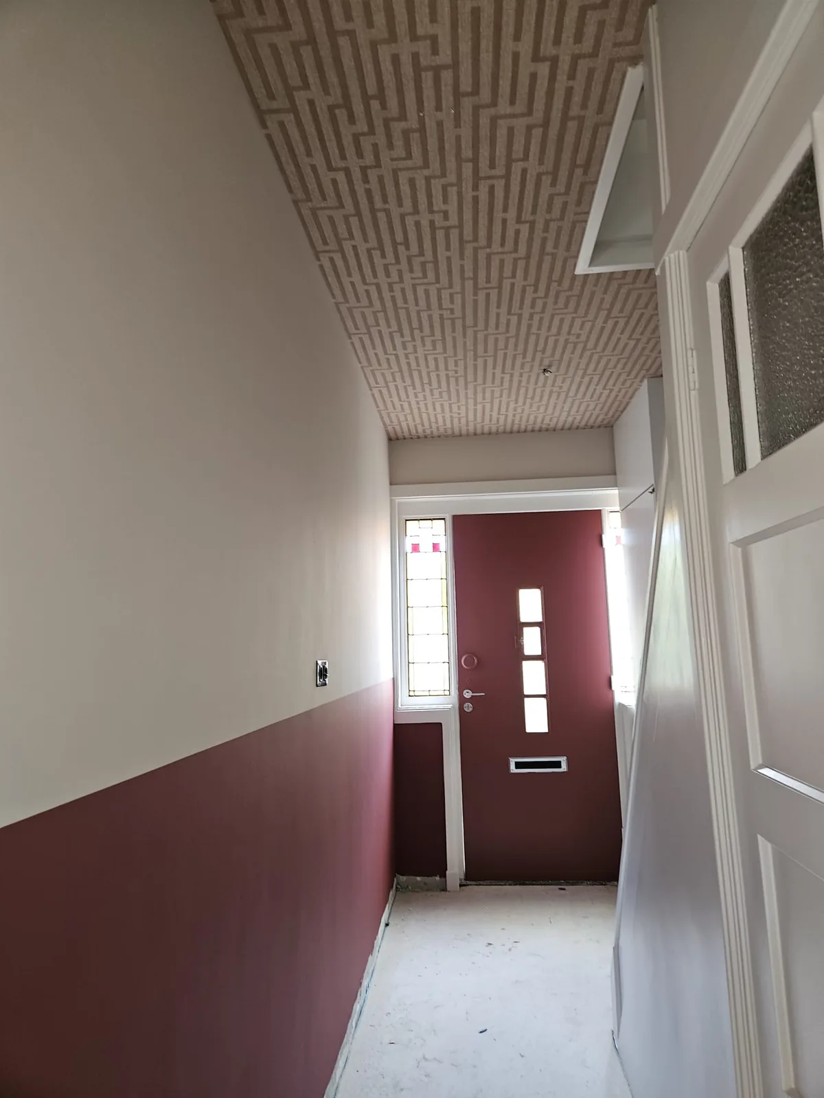 Hal met behangen plafond, donkerrode lambrisering en een rode voordeur