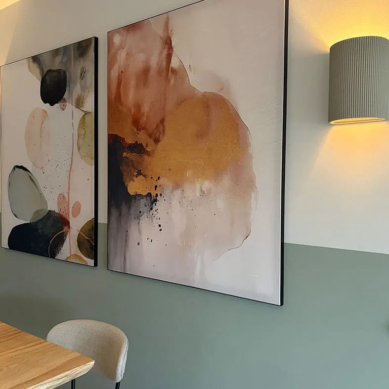 Twee abstracte schilderijen in zwarte lijst tegen een zeegroene wand