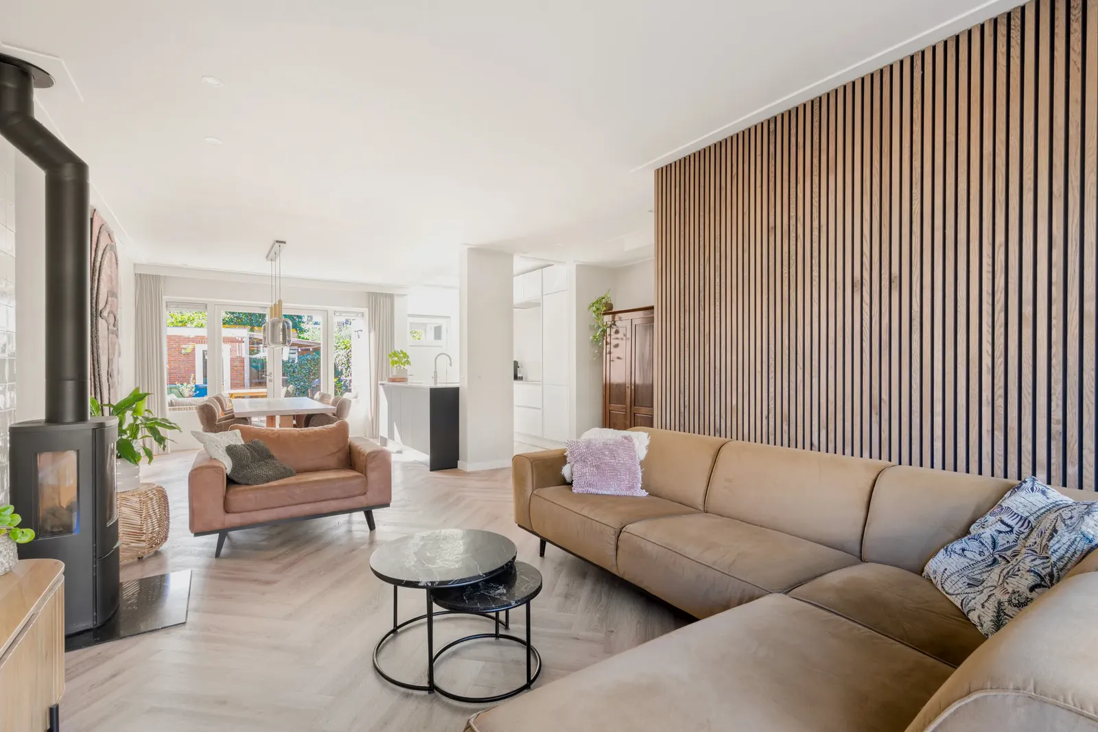 Woonkamer met een cognac hoekbank, een wand van houten latten en een houtkachel