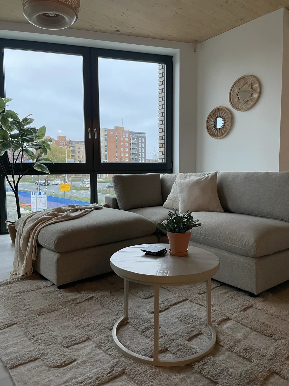 Woonkamer van de modelwoning met hoekbank, ronde salontafel en zicht op de nieuwbouw
