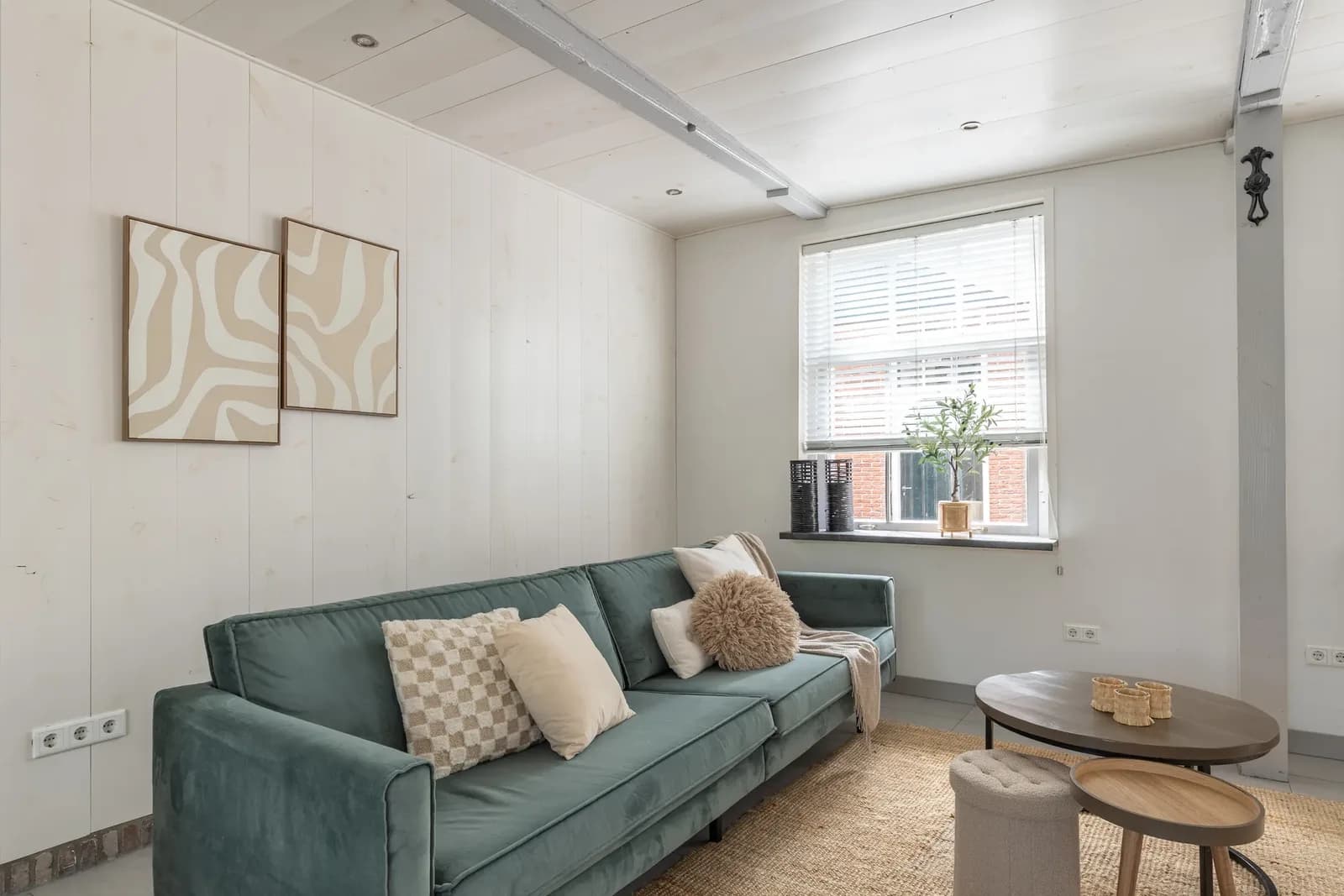 Woonkamer met groene fluwelen bank, twee abstracte prints op de houten wand en een ronde salontafel